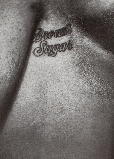 A close-up photo of a person's chest. Between their breasts is a tattoo that says "brown sugar."
