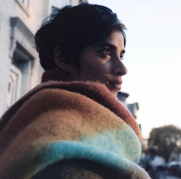 A headshot of Fahira Roisin. She is Bangladeshi. She has short black hair. She has a large colorful blanket wrapped around her. She is looking into the distance.