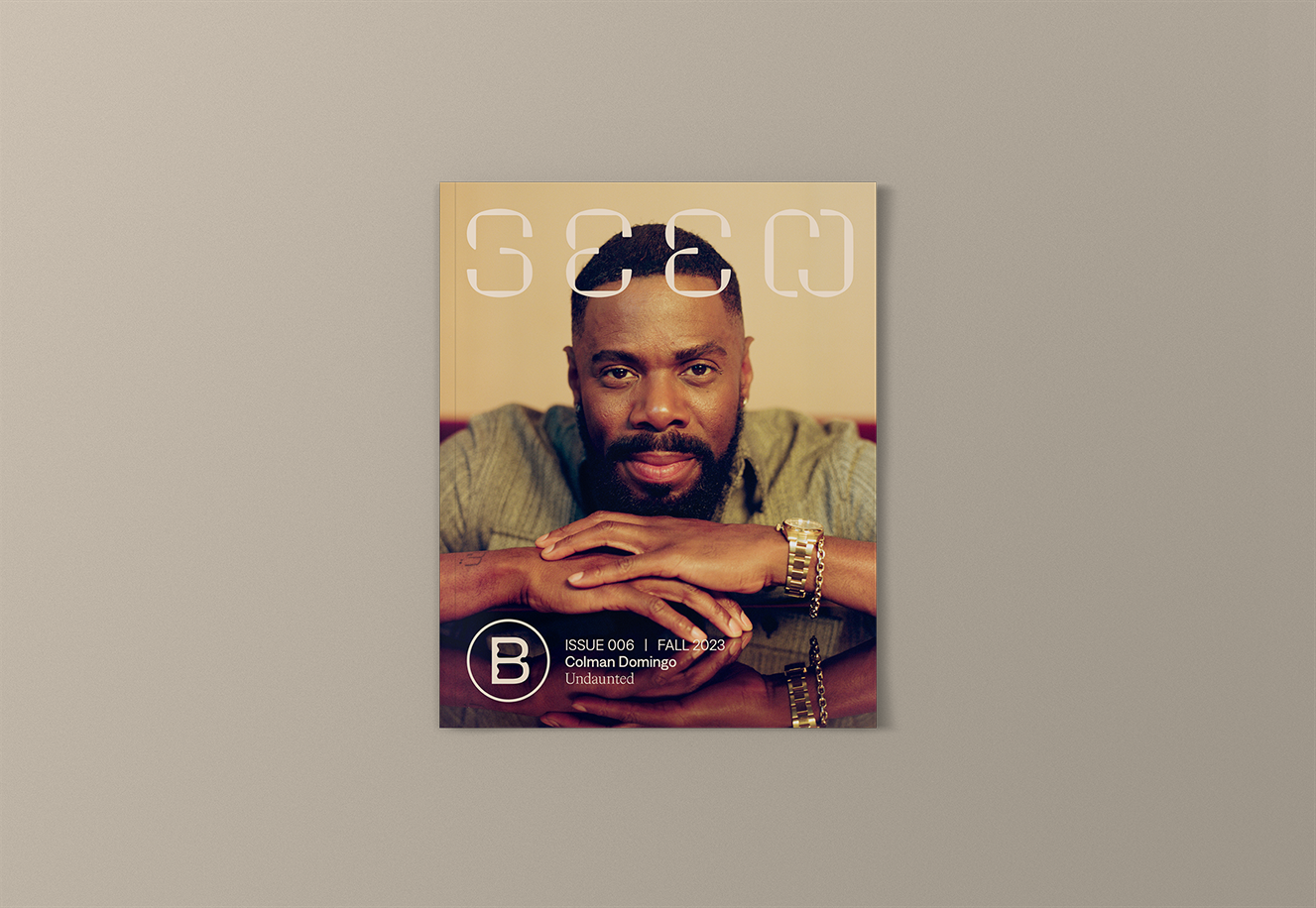 Seen Issue 006 with cover star Colman Domingo. Order and subscribe. Colman faces the camera directly, his chin rests on his hands which are crossed in front of him. He wears a gold watch and lightly colored shirt. His reflection is shown on the table upon which he rests his hands.