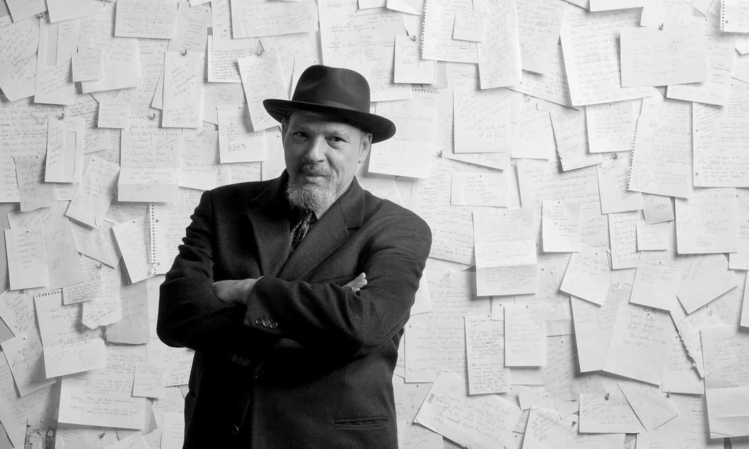 A film still from "The Ground on Which I Stand" shows the playwright August Wilson, in a sportscoast and top hat, with his arms folded, standing in front of a wall of paper notes.